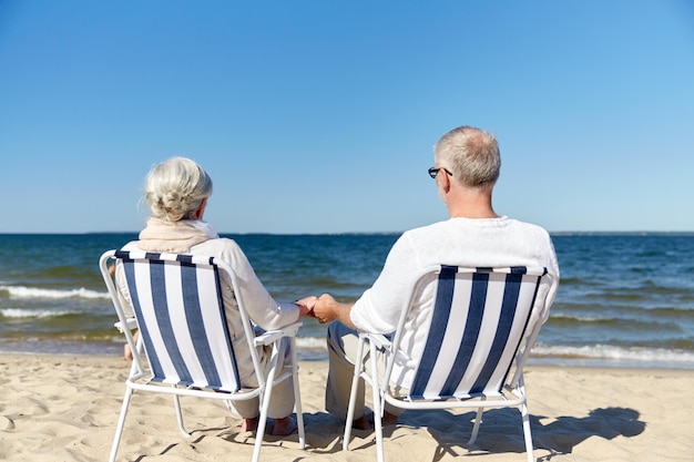 Foto familie, ouderdom, reizen, toerisme en mensenconcept - gelukkig senior paar zittend op ligstoelen op zomerstrand