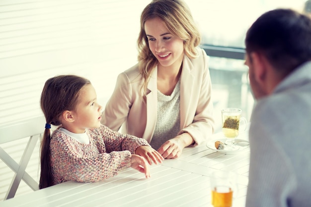 familie, ouderschap, communicatie en mensenconcept - gelukkige moeder, vader en klein meisje aan het eten en praten in restaurant of café