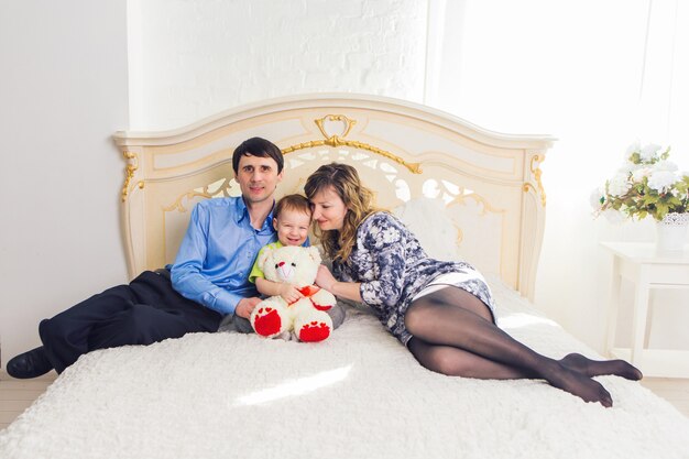 Familie, ouderschap en kinderen concept - portret van gelukkige moeder, vader en zoon die samen op bed in de slaapkamer thuis zitten.