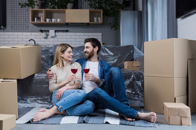 Familie paar verliefd man en vrouw zittend op de vloer vieren een nieuw huis in een nieuw appartement wijn drinken tussen kartonnen dozen