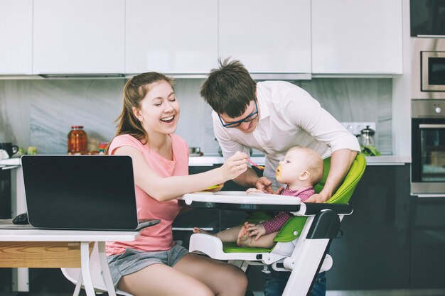 Familie pappa en mamma voeden baby in de keuken gelukkig samen thuis lachend in de keuken