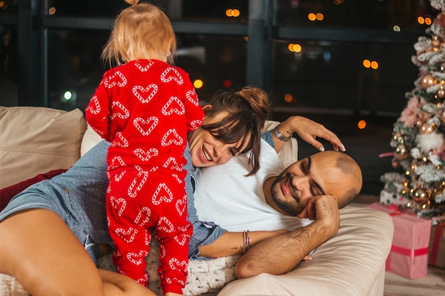 Familie plezier met Kerstmis op de bank met een klein kind in pyjama