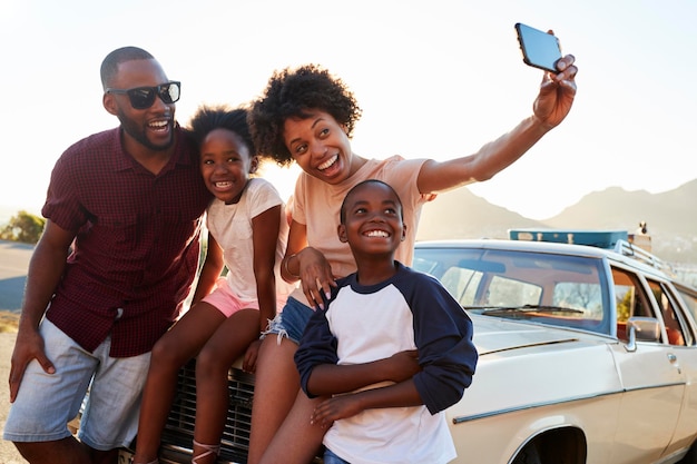 Familie poseert voor een selfie naast een auto die is ingepakt voor een reis