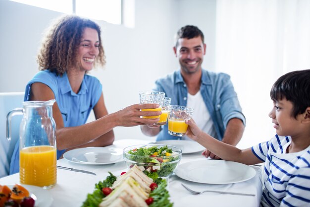 Familie roosterende glazen jus d'orange terwijl het hebben van ontbijt