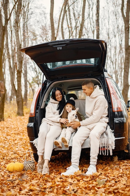 Familie rust na een dag buiten doorbrengen in het herfstpark Vader moeder hun dochter en hond zitten in de kofferbak glimlachend Familie dragen beige sportieve kostuums