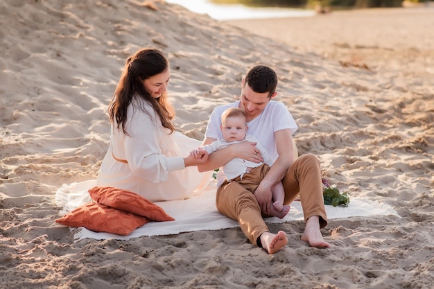 Familie rust op een picknick op het strand in de buurt van de zee oceaan moeder en vader houden een kind een gelukkig gezin