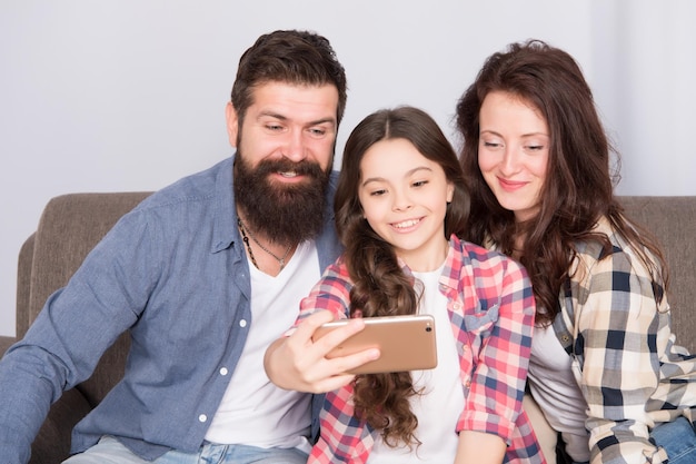 Familie selfie Familie brengt samen weekend door Smartphone gebruiken voor selfie Vriendelijke familie die samen plezier heeft Moeder, vader en dochter ontspannen op de bank Familie poseren voor foto Leg gelukkige momenten vast