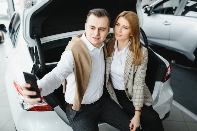 Familie selfie in dealer. Gelukkig jong koppel kiest en koopt een nieuwe auto voor het gezin.