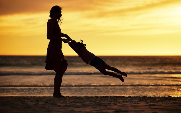 Familie silhouet en zonsondergang op het strand met moeder zwaaiend kind tegen gele lucht met liefde, zorg en ondersteuning op vakantie in de zomer Vrouw en kind over zee voor reisplezier, avontuur en vrijheid