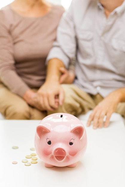 Familie, spaargeld, leeftijd en mensen concept - close-up van senior koppel met munten geld en spaarvarken op tafel