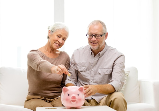 familie, spaargeld, leeftijd en mensen concept - glimlachend senior koppel met geld en spaarvarken thuis