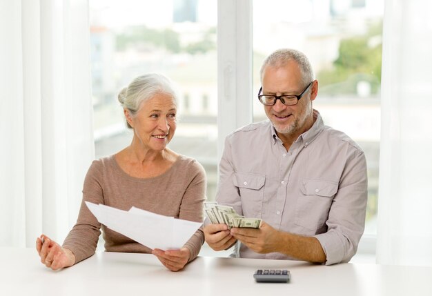 Foto familie, spaargeld, leeftijd en mensen concept - glimlachend senior koppel met papieren, geld en rekenmachine thuis