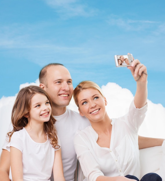 familie, technologie en mensen - glimlachende moeder, vader en klein meisje maken selfie met camera over blauwe lucht en witte wolkenachtergrond