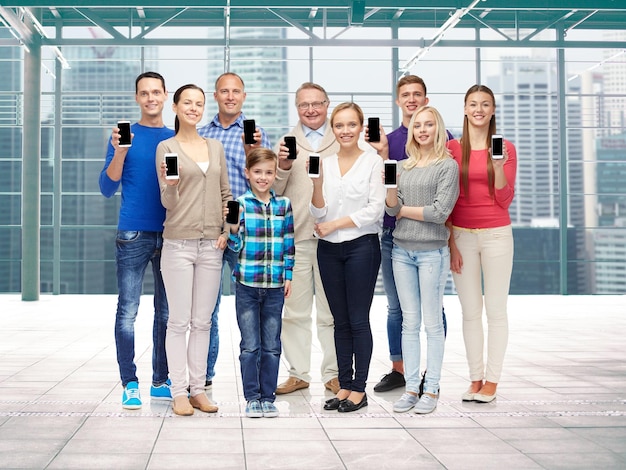 familie, technologie, generatie en mensenconcept - groep glimlachende mannen, vrouwen en jongen die smartphones tonen over terminal met de achtergrond van het vensterstadszicht