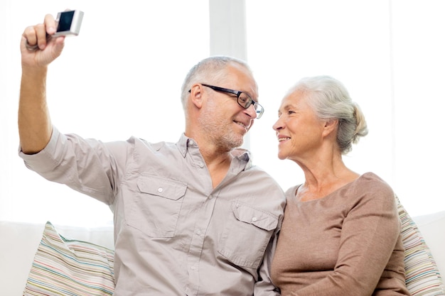 familie, technologie, leeftijd en mensenconcept - gelukkig senior paar dat thuis selfie met camera neemt