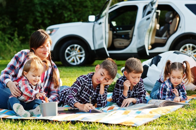 Familie tijd samen doorbrengen. Moeder met vier kinderen buiten in picknickdeken tegen hun amerikaanse suv.