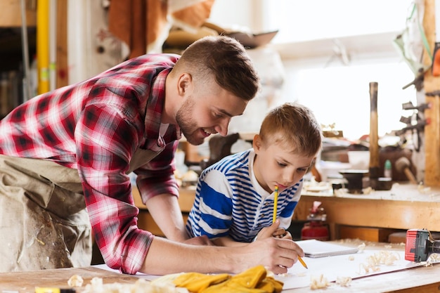 familie, timmerwerk, houtbewerking en mensenconcept - gelukkige vader en zoontje met blauwdruk op workshop