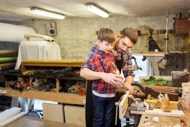 Foto familie, timmerwerk, houtbewerking en mensenconcept - vader en zoontje met hamer en beitel werken met houten plank in werkplaats