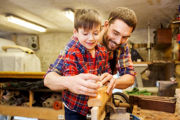 familie, timmerwerk, houtbewerking en mensenconcept - vader en zoontje met vliegtuig werken met houten plank in werkplaats