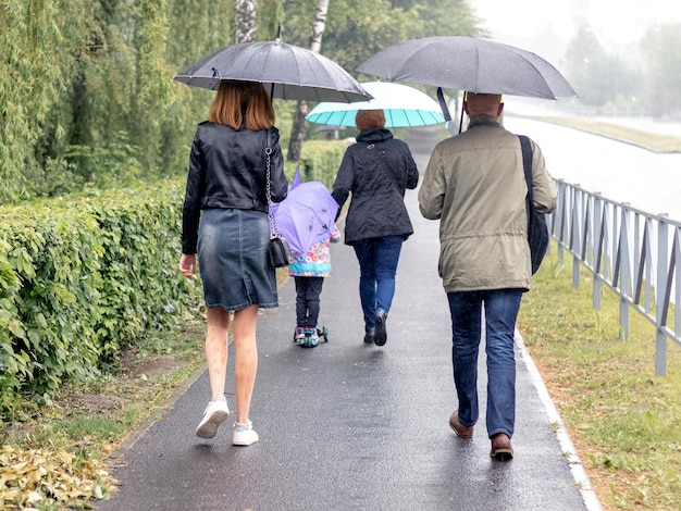 Familie vader moeder en kinderen wandelen in het park onder paraplu's bij regenachtig weer