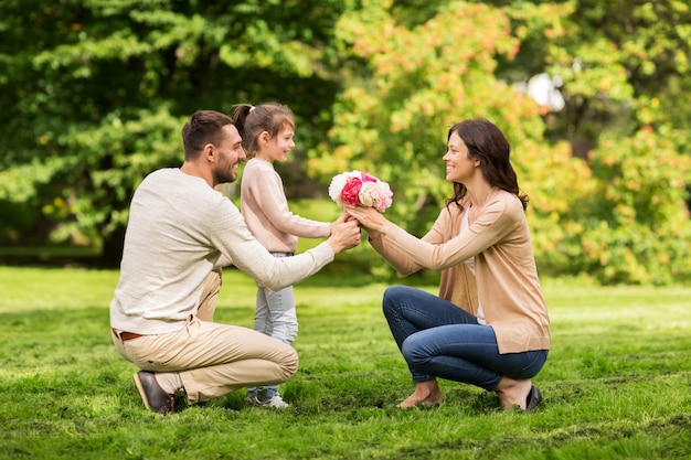 familie, vakantie en mensenconcept - gelukkige vader en meisje die bloemen geven aan moeder in zomerpark