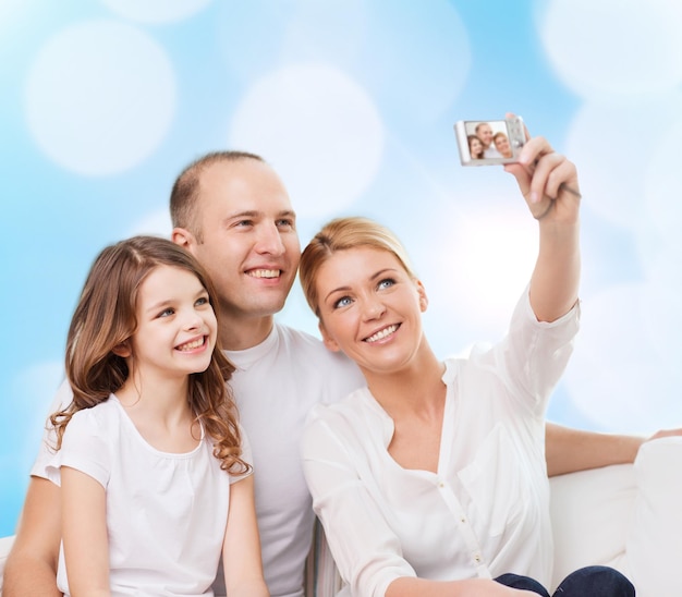 familie, vakantie, technologie en mensen - glimlachende moeder, vader en klein meisje maken selfie met camera over blauwe lichtenachtergrond