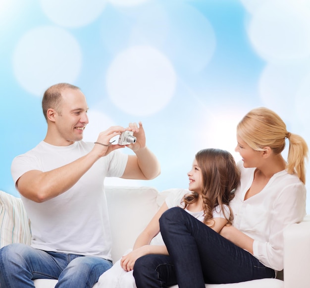 familie, vakantie, technologie en mensen - glimlachende moeder, vader en klein meisje met camera over blauwe lichtenachtergrond