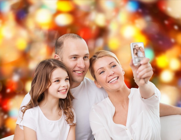 familie, vakantie, technologie en mensenconcept - glimlachende moeder, vader en meisje die selfie met camera over rode lichtenachtergrond maken