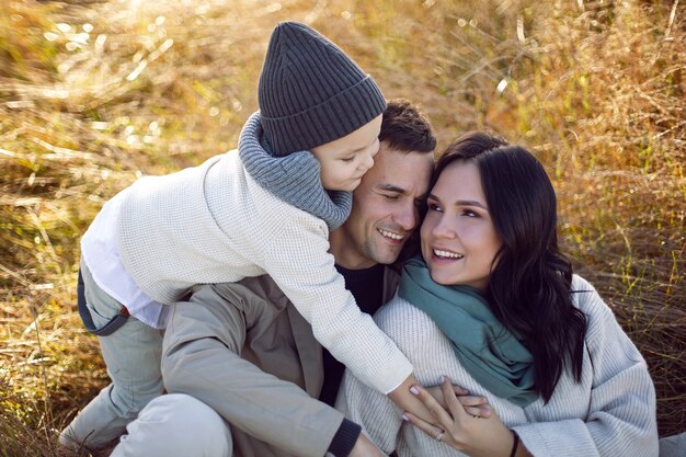 Familie van drie met een jongenskind, mama en papa liggen op een veld in de herfst bij zonsondergang