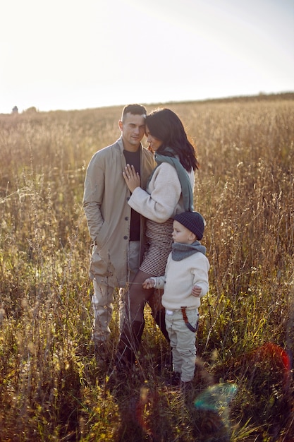 Familie van drie met een jongenskind, mama en papa staan in de herfst op een veld bij zonsondergang