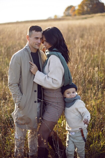 Familie van drie met een jongenskind, mama en papa staan in de herfst op een veld bij zonsondergang
