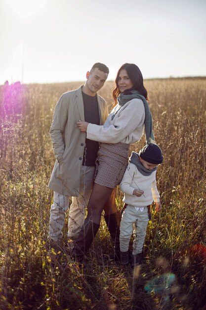 Familie van drie met een jongenskind, mama en papa staan in de herfst op een veld bij zonsondergang