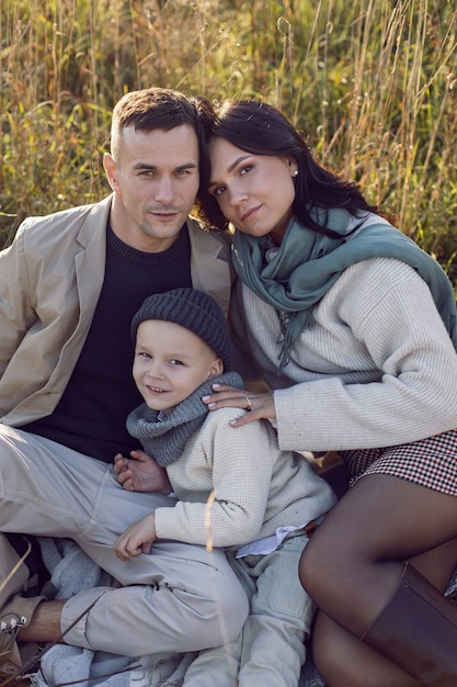 Foto familie van drie met een jongenskind, mama en papa zitten op een veld in de herfst bij zonsondergang