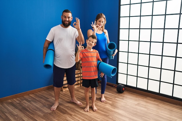 Familie van drie met yogamat die ok teken met vingers doet, glimlachend vriendelijk gebarend uitstekend symbool