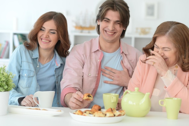 Familie van drie samen tijd doorbrengen aan tafel met koekjes en thee