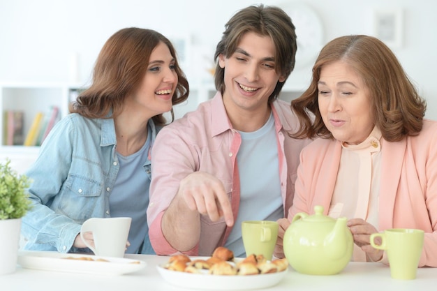 Familie van drie samen tijd doorbrengen aan tafel met koekjes en thee
