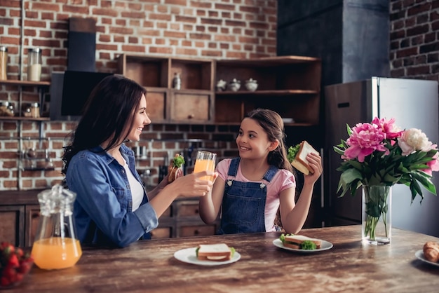 Familie van moeder en dochter die sandwiches met jus d'orange eten voor ontbijt in de keuken