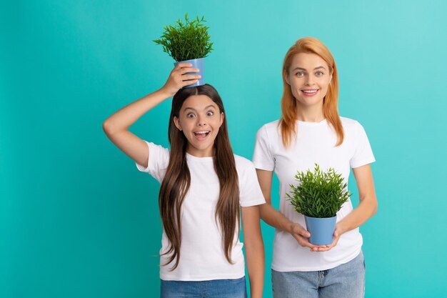 Familie van moeder en verrast meisje dat een potplant op het hoofd houdt om een grotere blauwe achtergrond te laten groeien