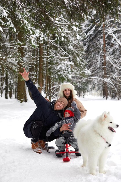 Familie van moeder, vader en zoon die plezier hebben in besneeuwd winterhout met vrolijke hond