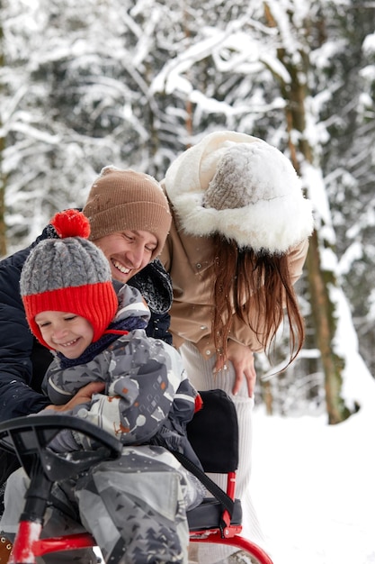 Familie van moeder, vader en zoon die plezier hebben in besneeuwd winterhout met vrolijke hond