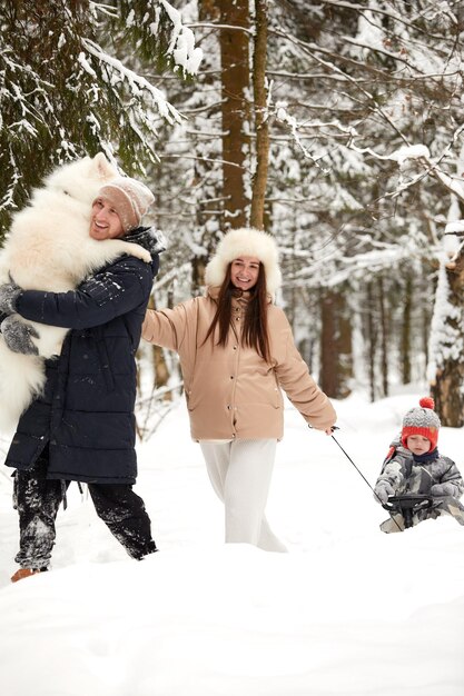 Familie van moeder, vader en zoon die plezier hebben in besneeuwd winterhout met vrolijke hond