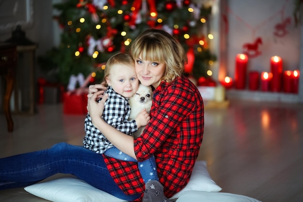 Familie van twee mensen moeder en op oudejaarsavond in de buurt van de versierde kerstboom zittend op de vloer met een klein huisdier.