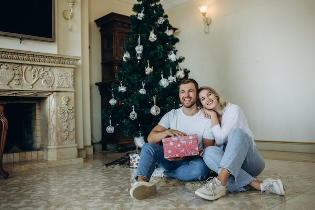 Familie van vier ouders, zwangere mama en papa en twee broers en zussen, kleine jongen en meisje in stijlvolle kleding in chalet, zijn klaar om Kerstmis en Nieuwjaar te verwelkomen in de buurt van een kerstboom met cadeauverpakkingen