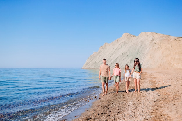 Familie van vier wandelen langs het strand op zomervakantie