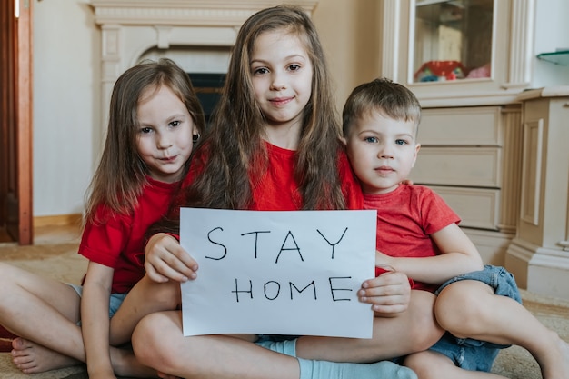 Familie verblijf thuis concept. drie kinderen met een bordje 'blijf thuis' voor bescherming tegen virussen en zorg voor hun gezondheid vanaf covid-19. quarantaine concept.