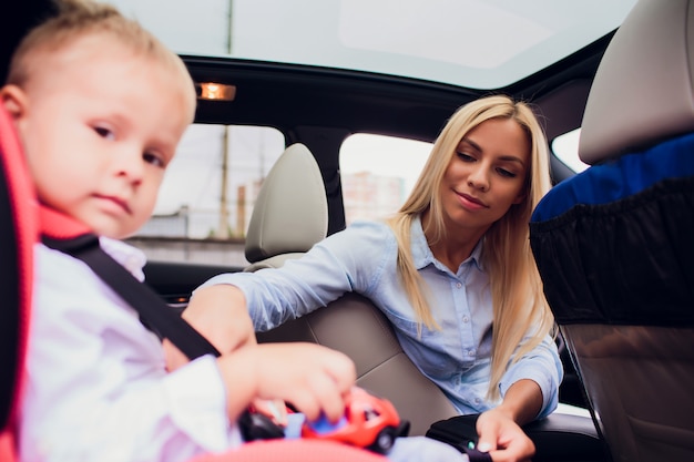 Familie, vervoer, wegreis en mensenconcept - gelukkig vrouwen vastmakend kind met veiligheidsgordel in auto