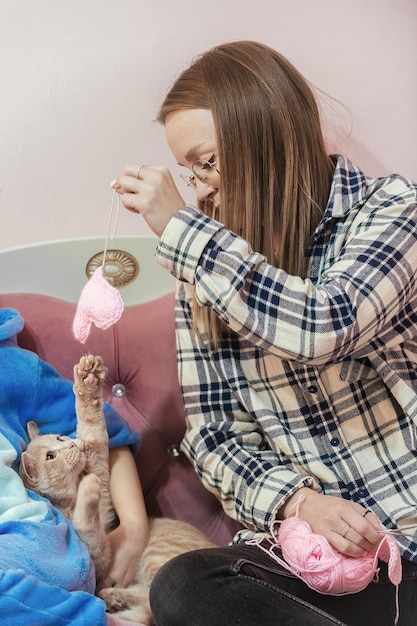 Familie vrije tijd met huisdieren, een jonge vrouw breit roze harten van garen op breinaalden