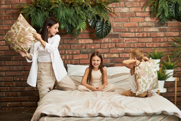 Familie vrije tijd. Moeder zoon en dochter vechten op kussens op het bed in de slaapkamer. Vreugde en plezier