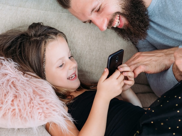 Familie vrijetijdsbesteding. papa en zijn kleine meisje kijken naar grappige clips op de mobiele telefoon. vreugde en gelach. gelukkige relatie. vader en kind communicatie.