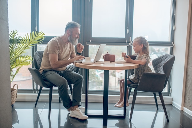 Familie weekend. Een man en zijn dochter zitten aan tafel, man aan het werk, zijn dochter aan het eten